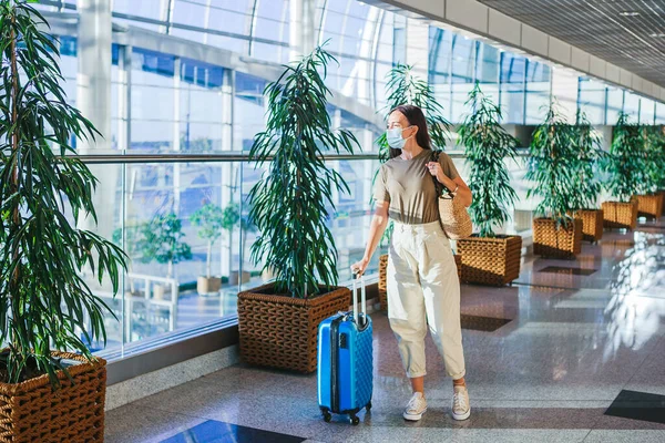 Jonge toeristische vrouw in medisch masker met bagage op de internationale luchthaven Stockfoto