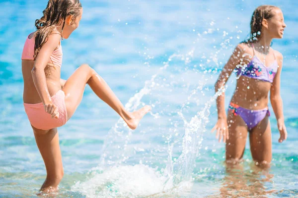 Mutlu çocuklar yaz tatilinde tropikal plajda dalgalara su sıçratıyorlar. Kızlar denizde oynar.