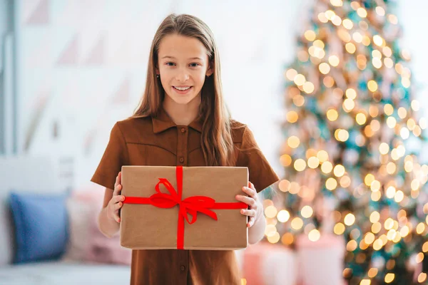 Back view of kid holds a gift box near the Christmas tree indoors. — Stock Photo, Image