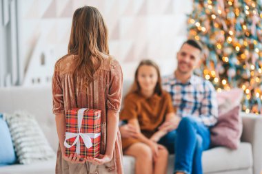 Arkaya bakan çocuk Noel ağacının yanında bir hediye kutusu tutuyor..