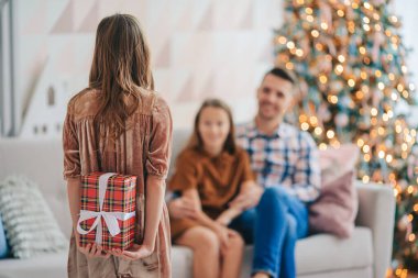 Yetenekli güzel küçük bir kız. Arkaya bakan çocuk, Noel ağacının yanında kapalı bir hediye kutusu tutuyor. Mutlu Noeller ve mutlu tatiller.