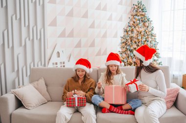 Genç anne ve küçük kızları Noel ağacının altında hediyelerle