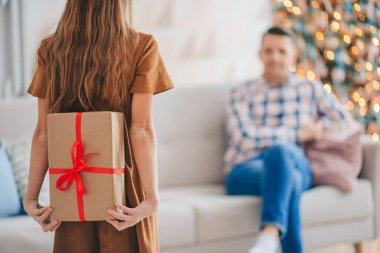 Arkaya bakan çocuk Noel ağacının yanında bir hediye kutusu tutuyor..