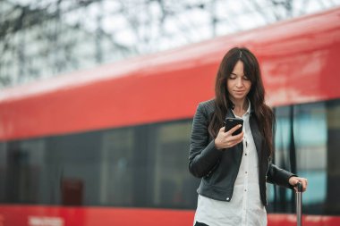 Bavullu genç bir kadın tren istasyonunda cep telefonuyla konuşuyor. Kafkasyalı turist seyahat ederken ekspres trenini bekliyor..