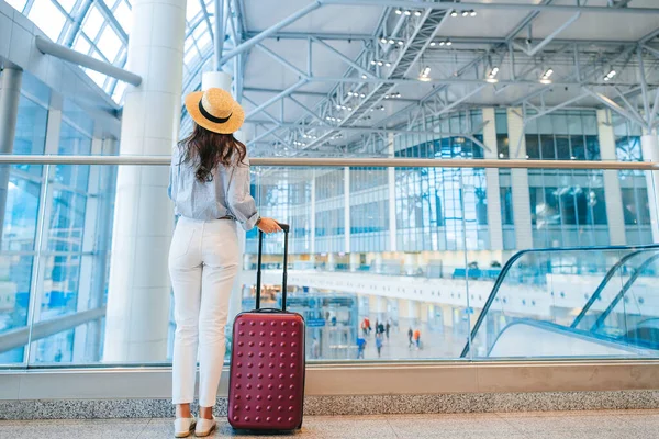 Young woman in hat with baggage in international airport waiting for flight aircraft