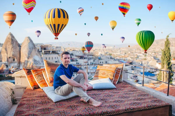 Young man on a rooftop with air balloons in the background in the blue sky in Goreme in Cappadocia, Turkey