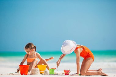 Küçük kızlar tropikal sahilde birlikte oynayıp kumdan kale yapıyorlar.