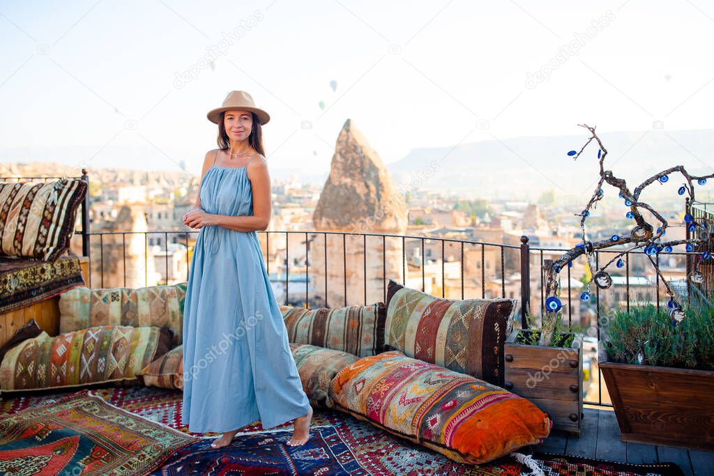 Woman on a rooftop with air balloons in the background in the blue sky in Goreme in Cappadocia, Turkey