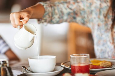 Woman pouring milk in mug from kettle. Breakfast time