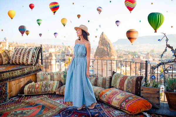 Woman on a rooftop with air balloons in the background in the blue sky in Goreme in Cappadocia, Turkey