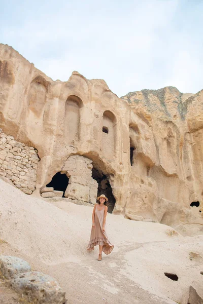 Young woman on background of ancient cave formations in Cappadocia, Turkey. The Monastery is one of the largest religious buildings.