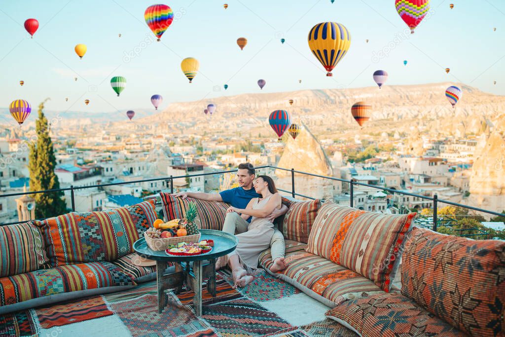 Happy couple on a rooftop on vacation in Cappadocia with hot air balloons in the background. Hot air balloon flights.