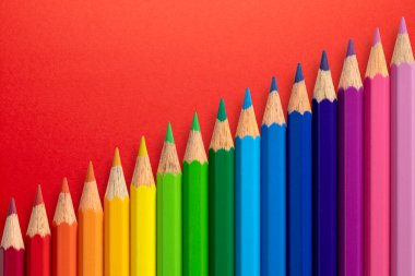 Kırmızı kağıt arkaplanda çapraz dizilmiş renkli kalemler.
