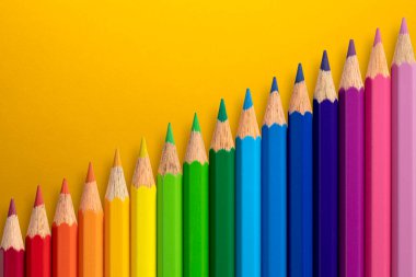 Sarı kağıt arkaplanda çapraz dizilmiş renkli kalemler.