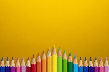 Sarı kağıttaki renkli kalemlerden yapılmış yaratıcı bir arka plan. Düz yatıyordu. Eğitim kavramı.