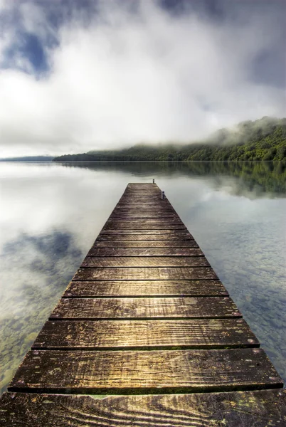 Lodí, přístavních mol táhnoucí se nad klidným jezerem se stoupající mlhou na kopcích, rotorua, Nový Zéland — Stock fotografie