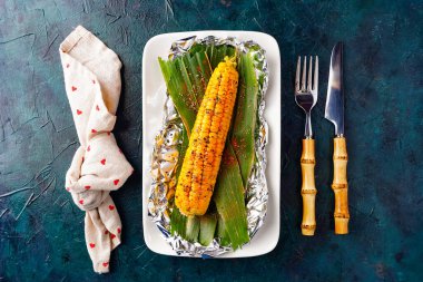 Tabakta ızgara baharatlı mısır koçanı, kırsal bir arka plan. Kavrulmuş tatlı mısırın üst manzarası.