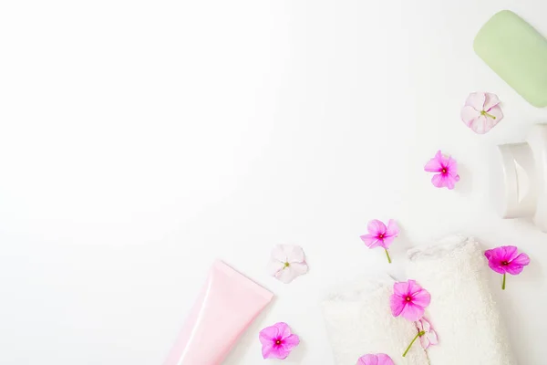 Spa sfondo bianco fiori rosa e una bottiglia di shampoo, sapone e crema lozione. Rotoli di asciugamano bianchi. Copia spazio al centro, spazio vuoto per il testo — Foto Stock