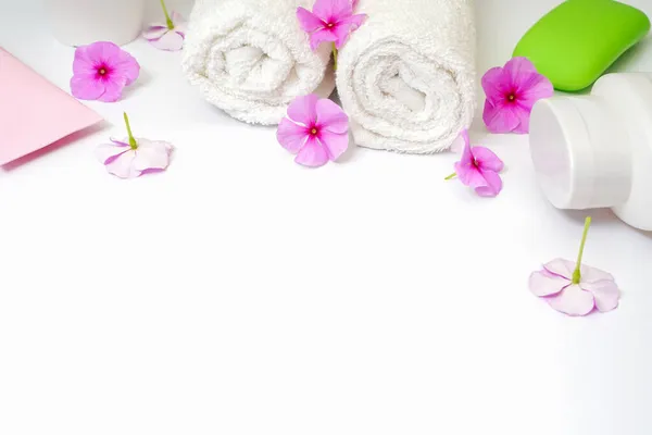 Spa sfondo bianco fiori rosa e una bottiglia di shampoo, sapone e crema lozione. Rotoli di asciugamano bianchi. Copia spazio al centro, spazio vuoto per il testo — Foto Stock