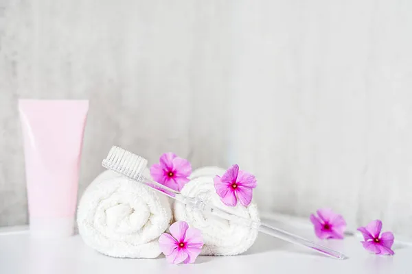 Brosse à dents, dentifrice et serviettes blanches, fleurs roses avec espace de copie. Aromathérapie et soins buccodentaires, hygiène corporelle et routines quotidiennes matinales. — Photo