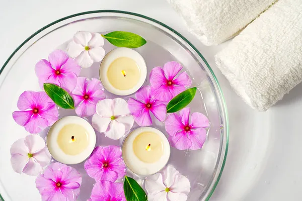Candele galleggianti ardenti con fiori rosa in una ciotola d'acqua e due asciugamani bianchi, relax spa, cura del corpo e benessere — Foto Stock