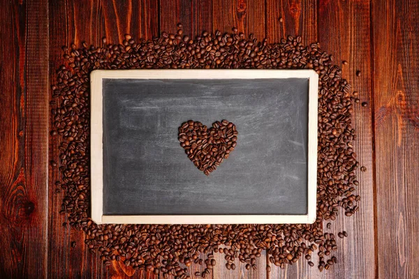 Coffee beans in the shape of heart on a black chalkboard, a lovers flower lovers for Valentines Day — Stock Photo, Image