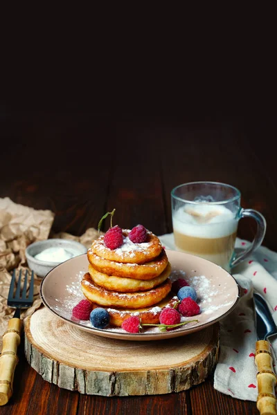 Delicious cheesecakes with sour cream and berries, raspberries and plums with powdered sugar topping. Delicious sweet dessert with cottage cheese. Copy space — Stock Photo, Image