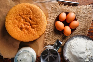 Tahta bir masa, un ve yumurta malzemelerinin üzerine ev yapımı mükemmel sünger keki.