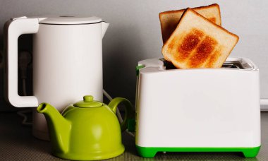 Beyaz su ısıtıcısı ve tost makinesi ahşap bir arka planda mutfak masasında duruyor.