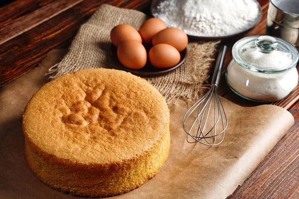 Homemade round sponge cake or chiffon cake on baking paper so soft and delicious with ingredients: eggs, flour, milk on wood table. Homemade bakery concept for background and wallpaper