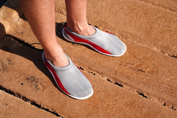 Protective neoprene shoes for coral and stones at sea. Aquashoes slippers for walking on corals. Legs of man in gray slippers, shoes for stones beach which protect foot on shore of pebbly beach sea — Stock Photo, Image