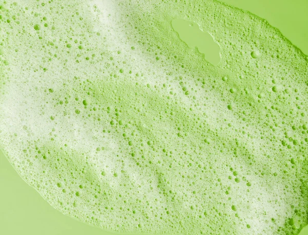 Face cleansing mousse sample. White cleanser foam bubbles on green background. Soap, shower gel, shampoo foam texture closeup.