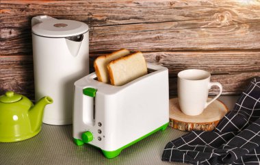 Beyaz su ısıtıcısı ve tost makinesi ahşap bir arka planda mutfak masasında duruyor.