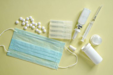 Tıbbi mavi maske, ampul tüpleri, haplar, burun spreyi ve hafif arka planda şırınga.