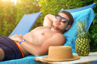 Rahat genç adam mavi iskemlede uyur, kumsalda poz verir, kırmızı güneş yanığı olur, güneşlenir ve bronzlaşır, yaz tatili ve tatil seyahati yapar. İnsanlar ve dinlenme