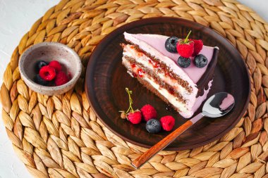Bir parça kek, krem peynirli çikolatalı bisküvi. Pembe krema süslemesi üzerine meyveler. Üst görünüm