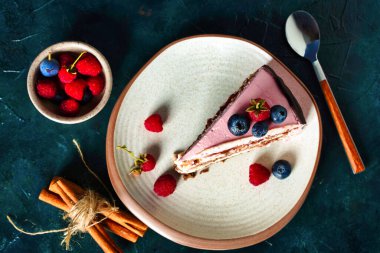 Koyu mavi arka planda krem peynirli çikolatalı bisküvi. Pembe krema süslemesi üzerine meyveler.