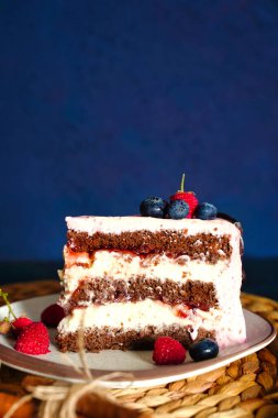 Koyu mavi arka planda krem peynirli çikolatalı bisküvi. Pembe krema süslemesi üzerine meyveler.