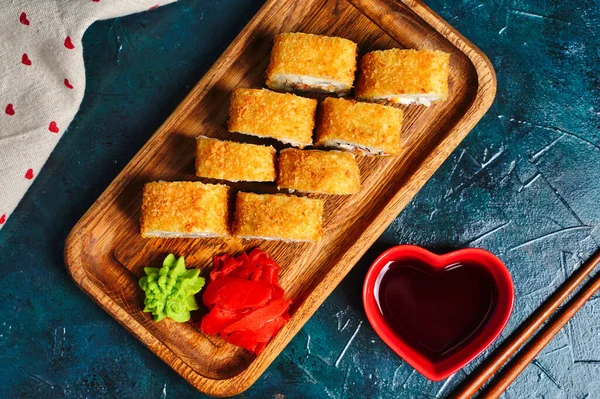 Gebratene Tempura-Sushi-Rollen auf einem Holzteller auf dunklem Hintergrund. Japanische traditionelle Fusionsküche. Ansicht von oben — Stockfoto