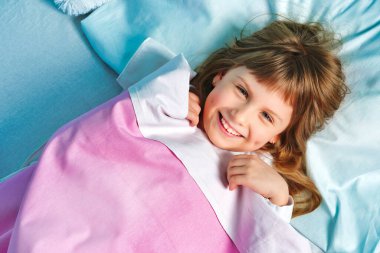 Neşeli liseli kız sabah uyandığında yatakta gülümsüyor. Sağlıklı bir uyku ve çocuklarda günlük rutin.