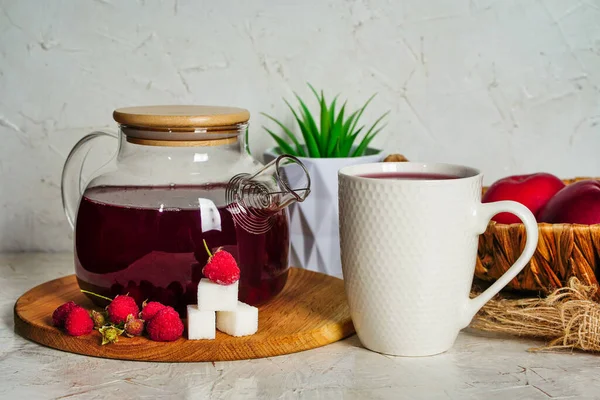 Raspberry tea in a transparent teapot with berries and sugar cubes, cup of tea