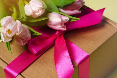 Pembe kurdeleli dekoratif hediye kutusu ve açık arkaplanda laleler.