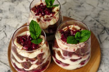 Kahverengi çikolatalı tatlı ve şeffaf bardakta beyaz krema. Pasta nane yaprağı ve doğum günü pastasıyla süslenmiş..