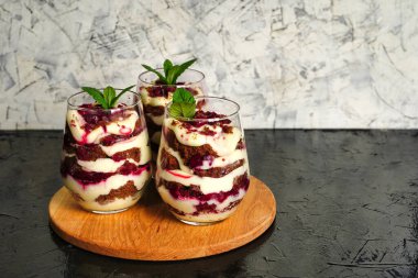 Kahverengi çikolatalı tatlı ve şeffaf bardakta beyaz krema. Pasta nane yaprağı ve doğum günü pastasıyla süslenmiş..