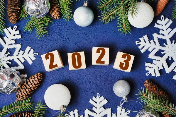 happy new year 2023 text sign on wooden cubes with frame of christmas tree branch and cones on blue background Snowflakes. High quality photo