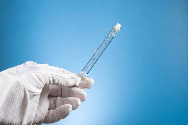 Linear halogen lamp with double base R7S. A gloved hand holds a lamp on a blue background.