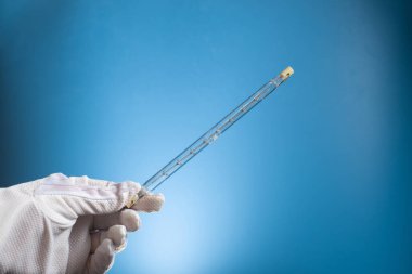 Çift tabanlı R7S ile doğrusal halojen lamba. Eldivenli bir el mavi arka planda bir lamba tutar..