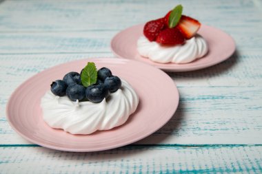 Çilekli ve böğürtlenli Pavlova keki ve pembe tabakta nane şekeri. Ev yapımı şekerleme. Eski beyaz ve mavi masa.