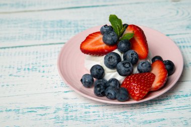 Çilekli ve böğürtlenli Pavlova keki ve pembe tabakta nane şekeri. Ev yapımı şekerleme. Eski beyaz ve mavi masa.