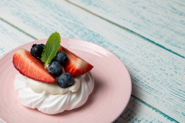 Çilekli ve böğürtlenli Pavlova keki ve pembe tabakta nane şekeri. Ev yapımı şekerleme. Eski beyaz ve mavi masa.